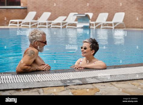 Happy Mature Couple In Sunglasses Chatting Inside Of Swimming Pool During Vacation Wellness