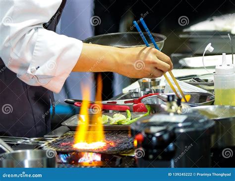 Chef Cooking With Flame In A Frying Pan On A Kitchen Stove Chef In Restaurant Kitchen At Stove