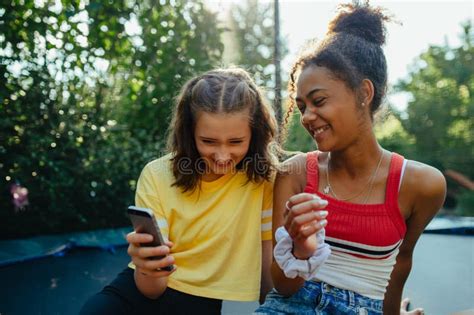 Teenager Girls Friends Spending Time Outdoors In Garden Laughing Sitting On Trampoline