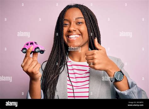 Young African American Girl Holding Small Car As Transport Insurance Over Isolated Pink