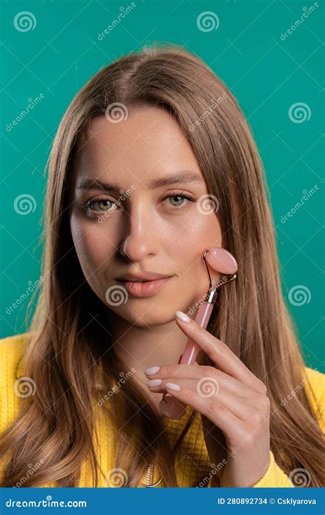 Young Woman Doing Face Massage With Rose Quartz Stone Roller On Blue