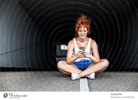 Redheaded Woman Sitting On Parking Level Holding Cell Phone A Royalty