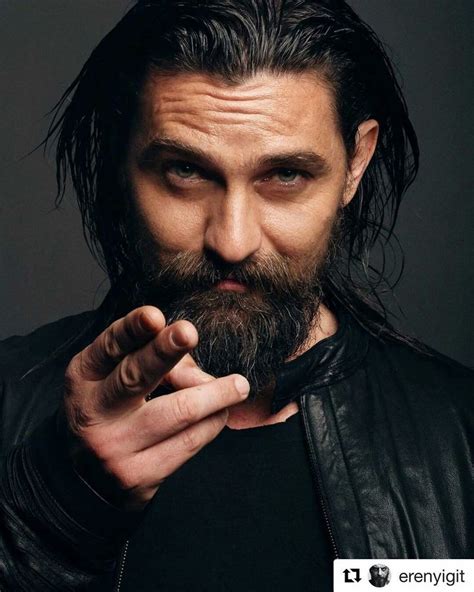 A Man With Long Hair And Beard Wearing A Leather Jacket Is Holding His