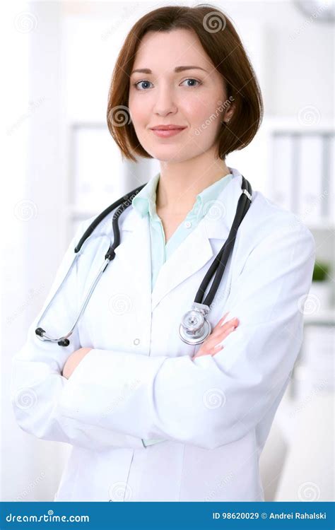 Young Brunette Female Doctor Standing With Arms Crossed And Smiling At