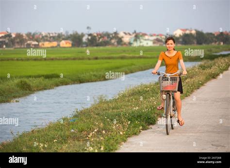 A Young Woman Rides A Bicycle Past A Rice Paddy In Hoi An Vietnam