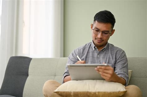 Premium Photo Focused Millennial Asian Man Using His Digital Tablet On Sofa In His Living Room