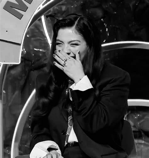 A Woman In A Suit And Tie Holding Her Hand To Her Mouth While Sitting On A Chair