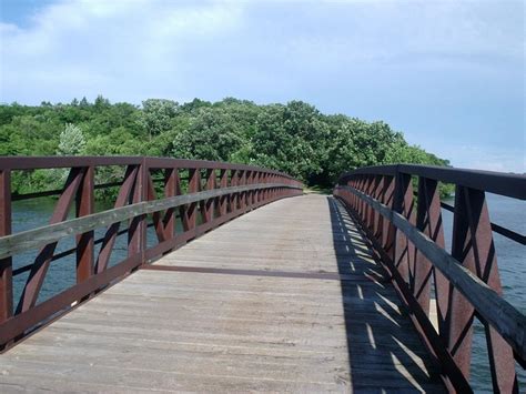 A Wooden Bridge Over Water With Trees On Both Sides And Blue Sky Above