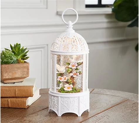 A White Birdcage Sitting On Top Of A Table Next To A Potted Plant