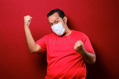 Young Asian Man Wearing A Medical Face Mask While Raise His Hand Up To