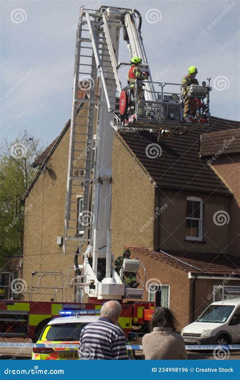 Two Firefighters Watch A Third Fireman Spraying Water On A Store In A