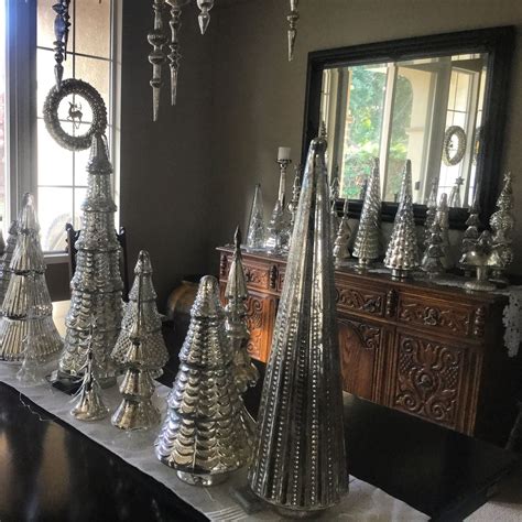 There Are Many Silver Christmas Trees On The Table In Front Of A Mirror And Window