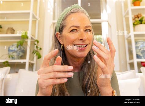 Smiling Mature Woman Gesturing With Hands On Video Call On Couch At