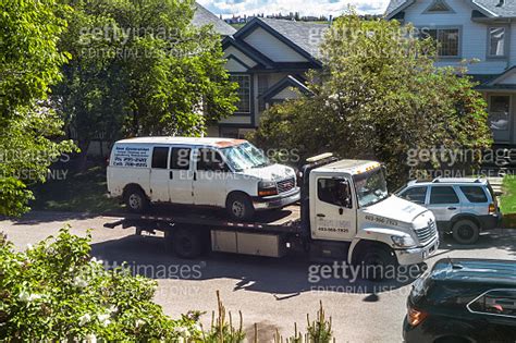 A White Delivery Van Being Towed By A Tow Truck On A Street For