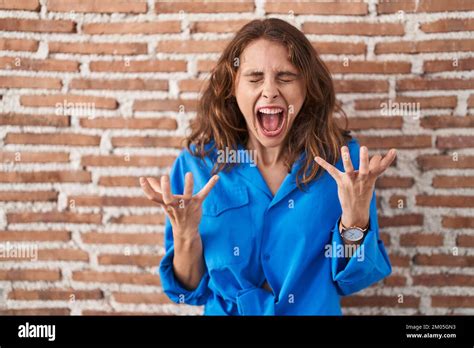 Beautiful Brunette Woman Standing Over Bricks Wall Celebrating Mad And Crazy For Success With