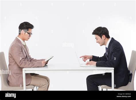 Side View Of Two Business Men Sitting At Table With A Book And A