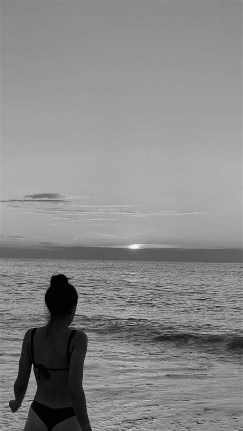 A Woman Standing On Top Of A Sandy Beach Next To The Ocean Under A Cloudy Sky