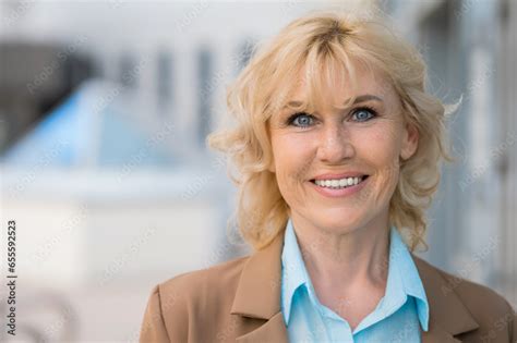 Mature Businesswoman In Formal Suit Smiles Posing At Camera On Blurred