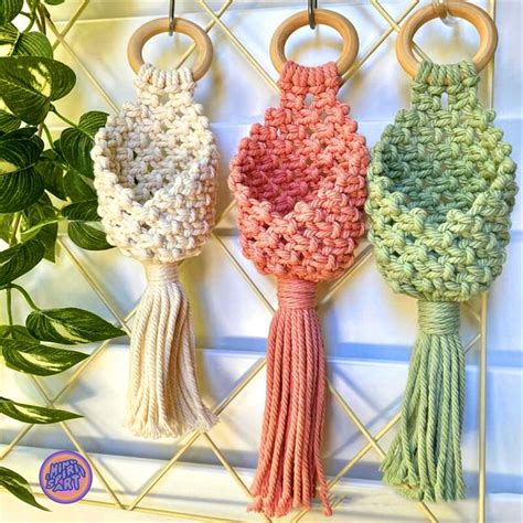 Three Crocheted Tassels Hanging On A Rack Next To A Potted Plant