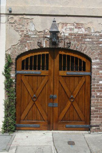 An Old Brick Building With Two Wooden Doors And A Lamp On The Wall Above It