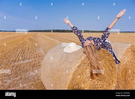 Une jeune fille blonde aux cheveux longs dans un chapeau blanc se repose et pose près des gerbes