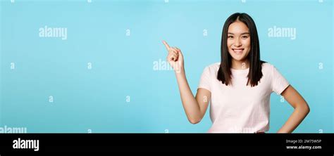Cute Smiling Asian Brunette Student Pointing At Upper Left Corner Showing Company Name Promo