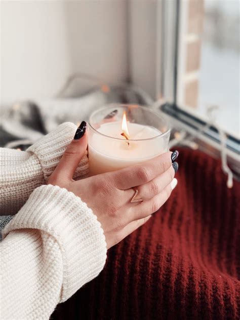 A Woman Holding A Lit Candle In Her Hand While Looking Out The Window