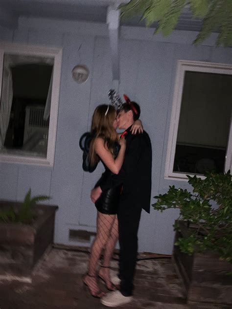 A Man And Woman Kissing In Front Of A Blue House At Night With The Lights On