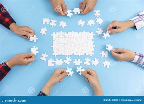 High Angle View Of Businesspeople Hand Solving Jigsaw Puzzle On A Blue