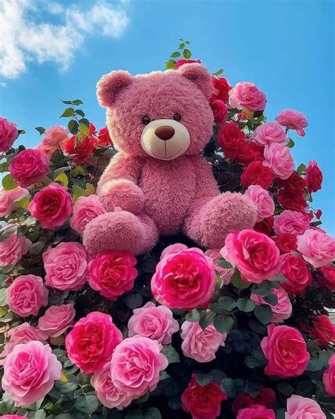 A Large Pink Teddy Bear Sitting On Top Of A Bush Filled With Red And