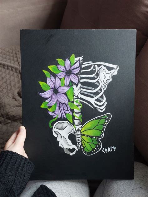 A Person Holding Up A Painting With Purple Flowers And A Green Skeleton