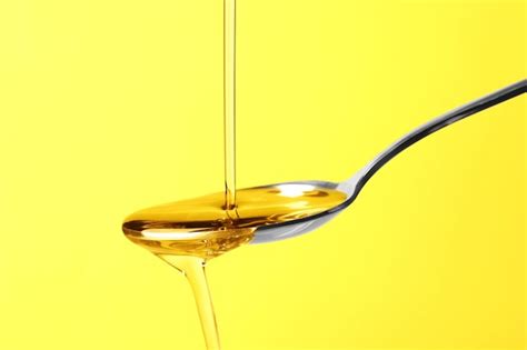 Premium Photo Pouring Cooking Oil Into Spoon On Yellow Background Closeup