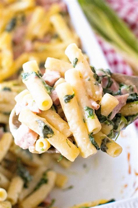 A Spoon Full Of Pasta With Ham And Spinach On It Is Being Held Up