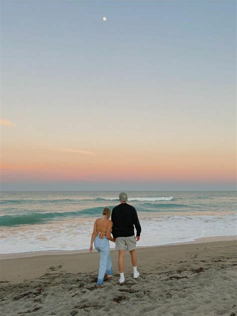 A Man And Woman Walking On The Beach At Sunset With An Ocean In The