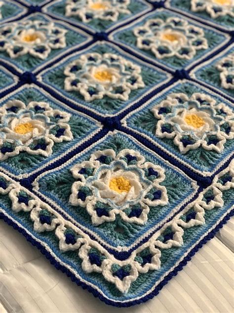 A Blue And White Crocheted Blanket With Flowers On It Sitting On A Bed