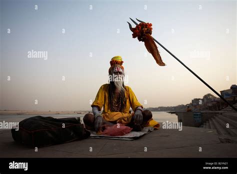 An Indian Sadhu Man Sits In Meditation Posture Near The Bank Of The