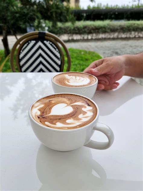The Right Hand Holding One Of Two Cups Of Hot Latte Art Coffee While
