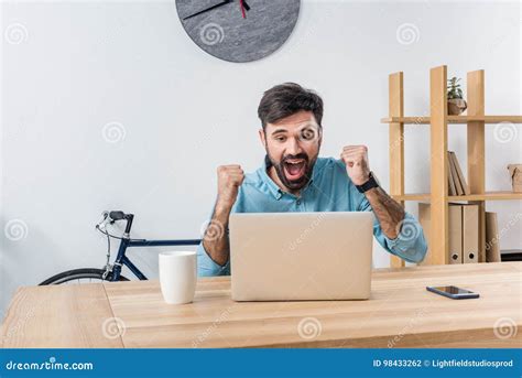 Excited Businessman Looking At Laptop At Workplace In Office Stock