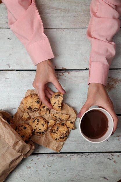 Manos femeninas sosteniendo una taza de café y galletas en la mesa de