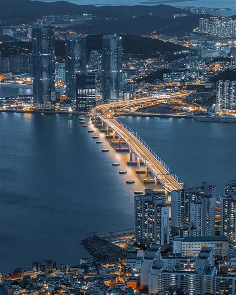 An Aerial View Of A City At Night With The Lights On And Bridge In The