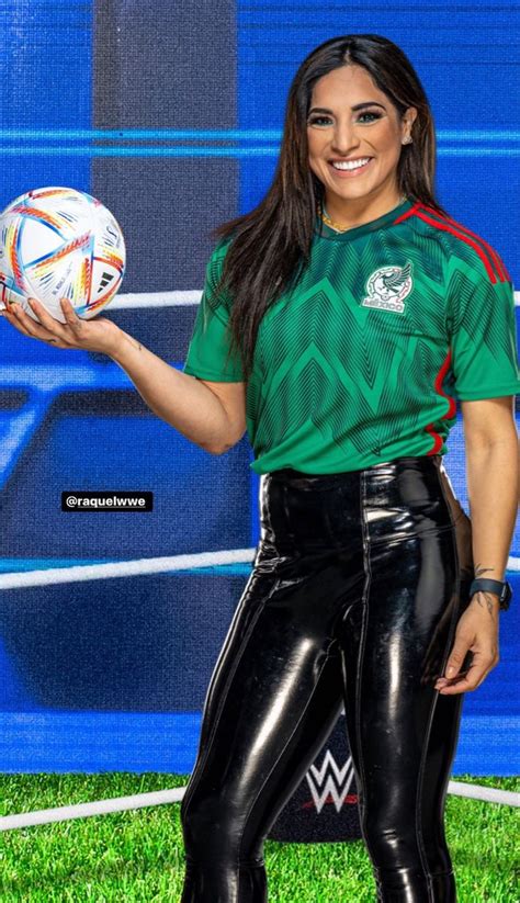 A Woman Holding A Soccer Ball In Front Of A Blue Wall And Green Grass Area