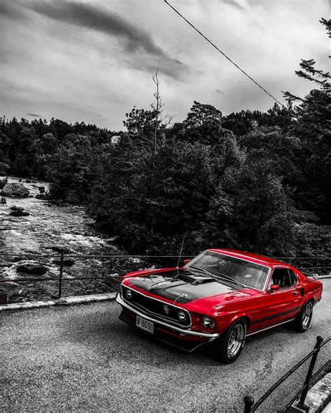 A Red Car Parked On The Side Of A Road Next To A Forest Filled With Trees