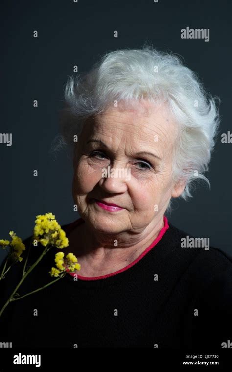 Authentic Portrait Of Grandmother Holding Yellow Flower On Dark Gray