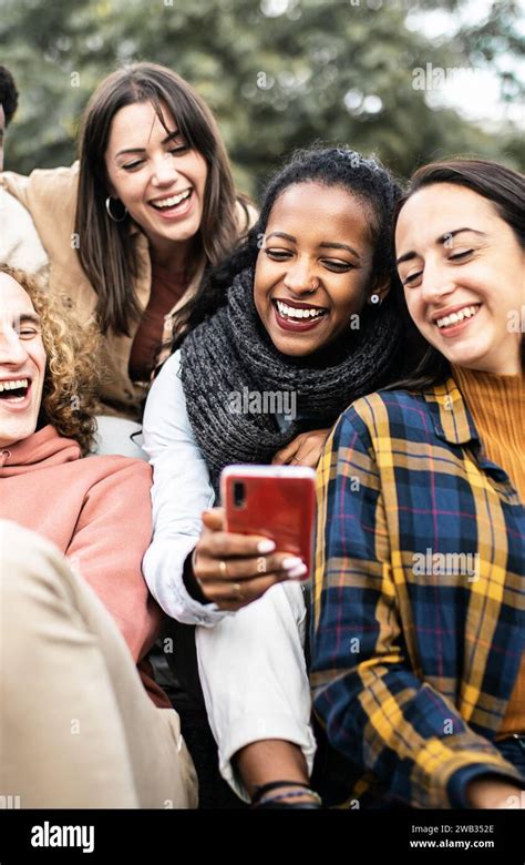 Millennial Multiracial Friends Using Smartphone While Sitting Outdoors