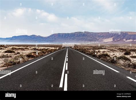 Long Straight Empty Asphalt Road Through Arid Landscape Against Ocean