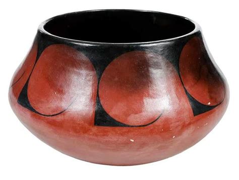 A Black And Red Vase Is Sitting On A White Surface With Circles Painted