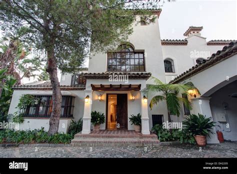 Tall Tree Beside Large Traditional Spanish Villa With Wall Lights On