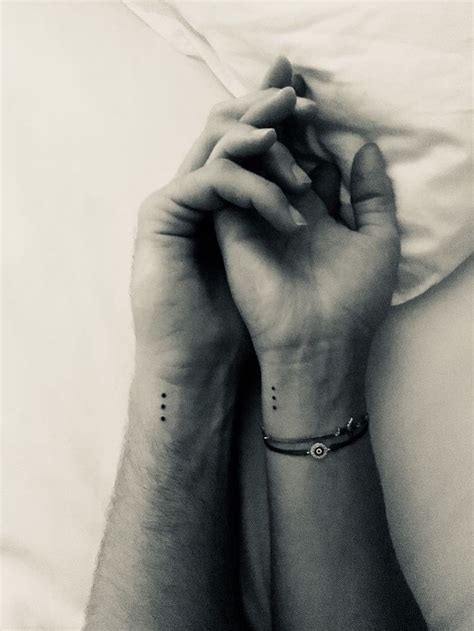 two people with matching tattoos on their arms holding each other's hands in bed