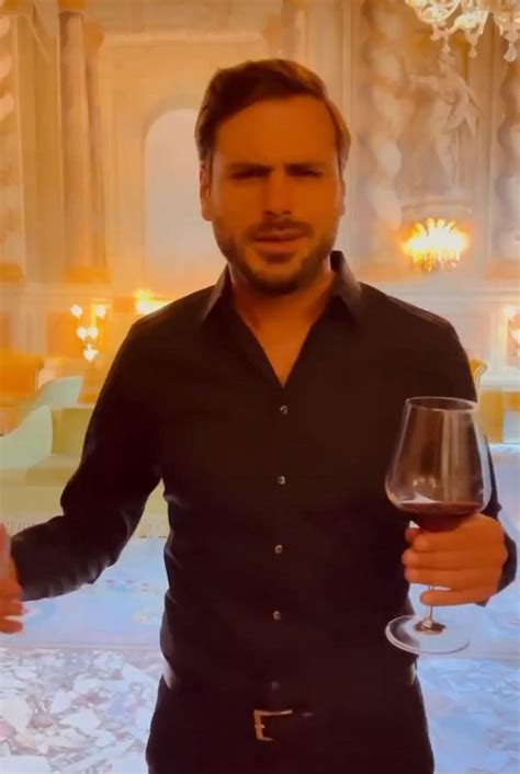 A Man Holding A Glass Of Wine In His Right Hand And Looking At The Camera