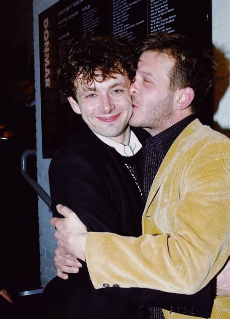 Two Men Hugging Each Other In Front Of A Wall